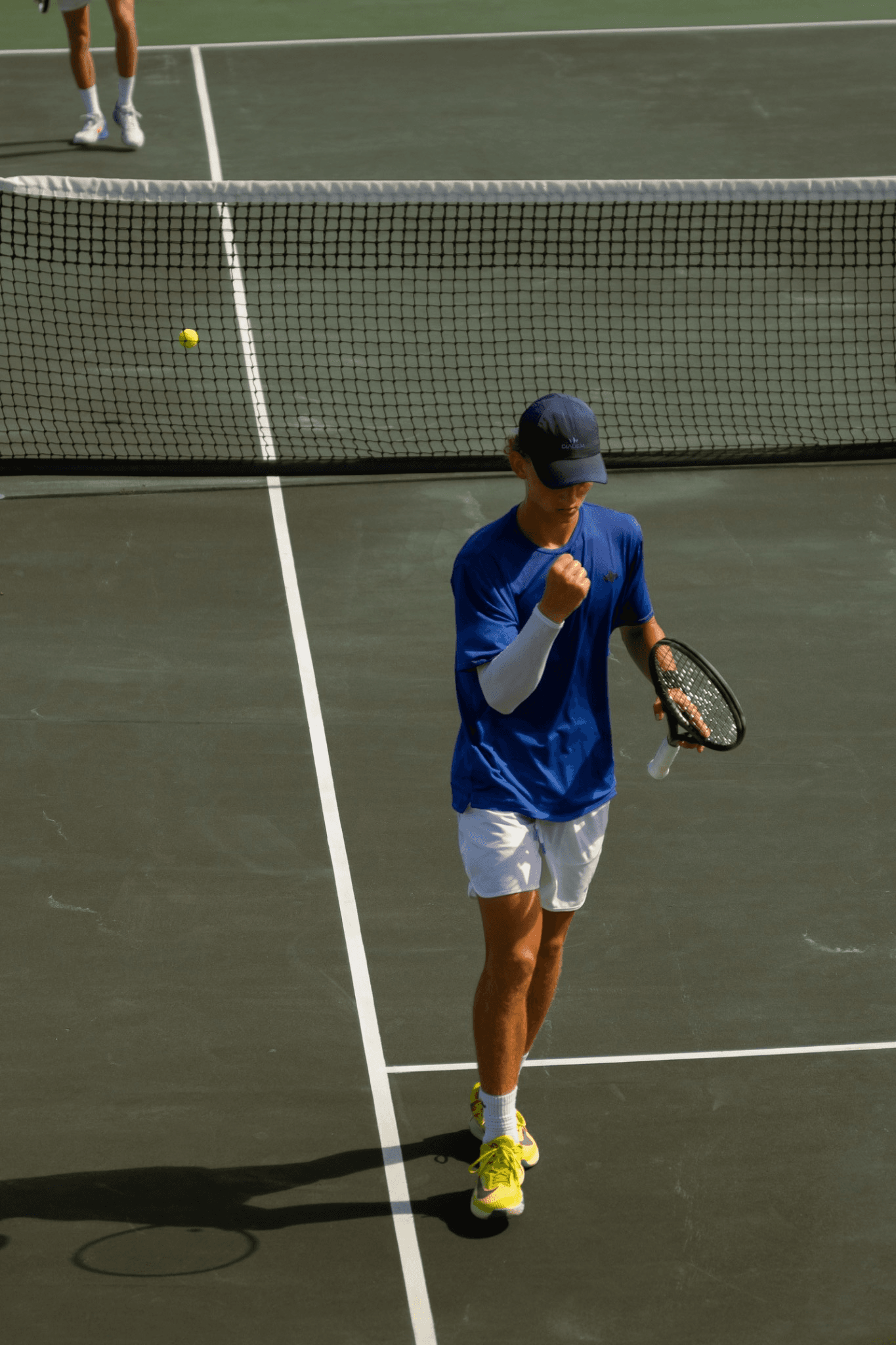 A player in a blue shirt and navy cap clenching a fist after a point